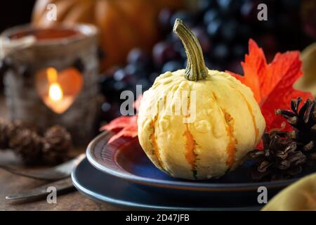 Autumnal Thanksgiving table setting with plates, silverware and traditional autumnal decorations like pumpkins, leaves, pinecones, grapes and a lanter Stock Photo