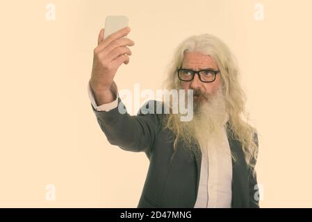 Studio shot of senior bearded businessman taking selfie picture with mobile phone Stock Photo