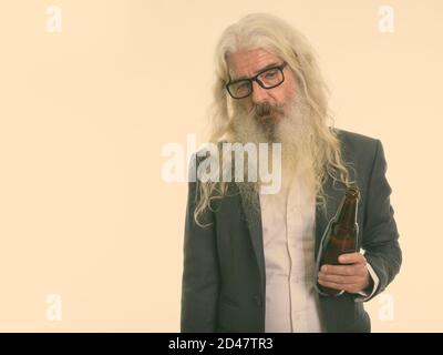 Studio shot of senior bearded businessman holding bottle of beer while looking sad Stock Photo