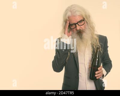 Studio shot of senior bearded businessman holding bottle of beer and looking tired Stock Photo