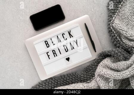 Creative top view flat lay promotion composition with text Black Friday on white Lightbox laying on grey laptop with black phone. Stock Photo