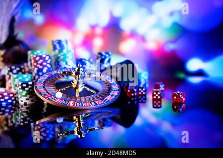 Casino concept.  Roulette wheel, poker chips and dice on shining table and on  colorful bokeh background. Stock Photo
