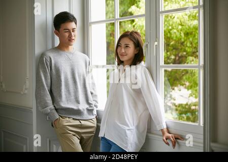 young asian couple standing by the window talking chatting during stay at home order Stock Photo