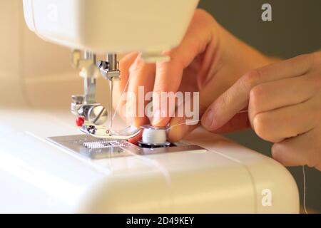 Preparing the sewing machine for work. Seamstress tucks thread into the eye of a needle. Installs the bobbin in the shuttle. Close up view. Stock Photo