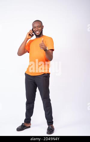young black man standing against a white background making a phone call, smiling and gives a thumbs up Stock Photo