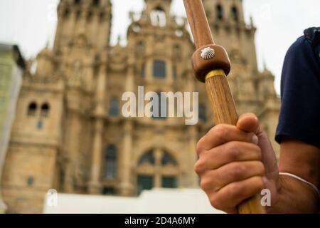 closeup of pilgrim hand holding walking stick with scallop shell, symbol of the camino de santiago pilgrimage, in front of the santiago cathedral Stock Photo