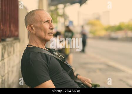 Profile view of bald senior tourist man thinking while waiting at the bus stop in Bangkok Thailand Stock Photo