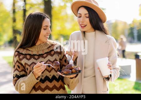two young and cheerful woman enjoying delicious cakes in city park in a positive and energetic mood Stock Photo