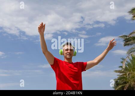 Happy man enjoys and smiles listening music with green earphones.Celebrating and smiling with happiness cheering with arms up.Happiness , freedom,succ Stock Photo