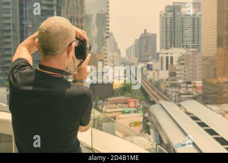 Back view of bald senior tourist man taking pictures of the view of the city in Bangkok Thailand Stock Photo