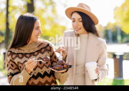 two young and cheerful woman enjoying delicious cakes in city park in a positive and energetic mood Stock Photo