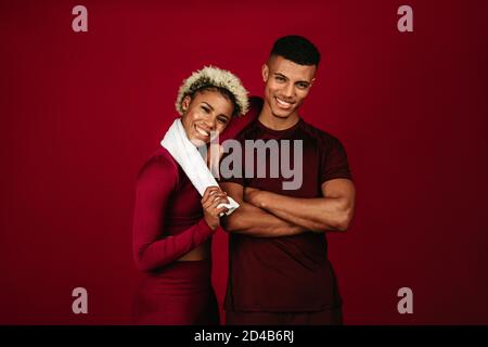 Cheerful african american couple in fitness wear standing together on maroon background. fitness couple relaxing after workout. Stock Photo