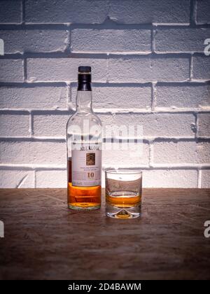 A half full bottle of Scottish whisky from the Aberlour distillery with a glass against a brick wall background Stock Photo