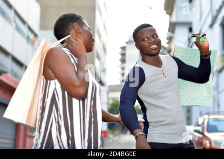 Happy couple on vacation with bags in town, woman holding her boyfriend by the hand and pulling him with colorful shopping packages. Stock Photo
