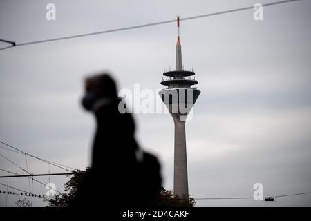 Duesseldorf, Germany. 09th Oct, 2020. A woman with a mouth-and-nose guard walks in front of the Rhine Tower in Düsseldorf. The corona pandemic is increasingly becoming a problem in the large cities and conurbations of North Rhine-Westphalia. Credit: Fabian Strauch/dpa/Alamy Live News Stock Photo