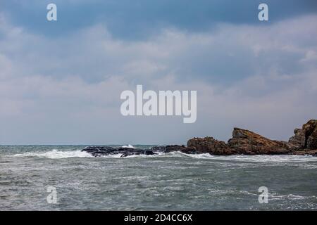 Dark moody autumn seascape landscape with few black birds, cormorants, resting on wet rock, stormy Black Sea, Bulgaria. Splashing sea waves and harsh cold windy weather Stock Photo