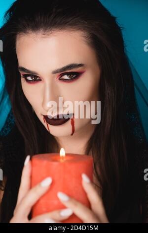 selective focus of brunette woman with blood on face holding burning candle on blue Stock Photo