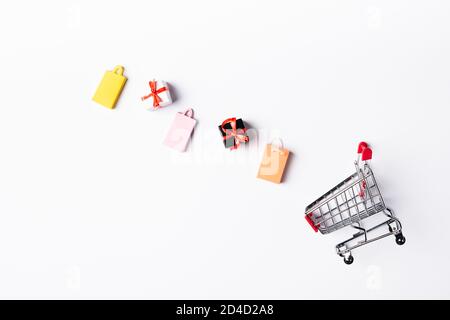 Top view of colorful toy shopping bags and gift boxes near cart on white background Stock Photo