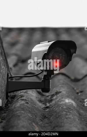 Home security concept. Black CCTV camera with glowing red bulb attached on house roof Stock Photo