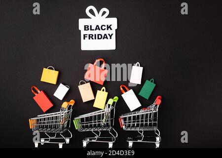 Top view of paper gift box with black friday lettering, toy carts and shopping bags on black background Stock Photo
