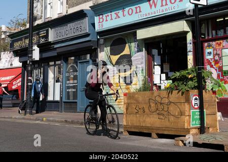 A female cyclist using a mobile phone whilst riding a bike on the Atlantic Road closure on the 16th September 2020 in Brixton in the United Kingdom. P Stock Photo