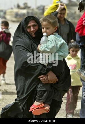 An Iraqi woman, a refugee from the Baghdad area, carries her son as she walks on a road south-east from the Iraqi capital April 5, 2003. A U.S. Marine commander said on Saturday American troops would use overwhelming force to crush any resistance if ordered to storm Baghdad and that the battle would cost many civilian lives.