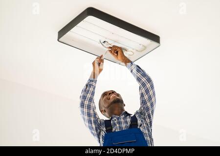 African Maintenance Electrician On Ladder Fixing And Installing Light Stock Photo