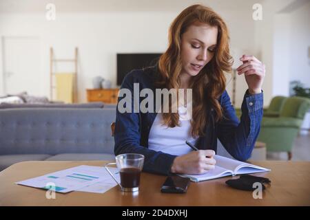 Woman taking notes while sitting on her desk at home Stock Photo