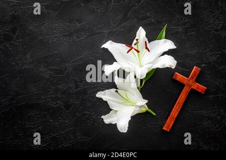 Funeral lily flowers with cross on dark stone background. Mourning symbols Stock Photo