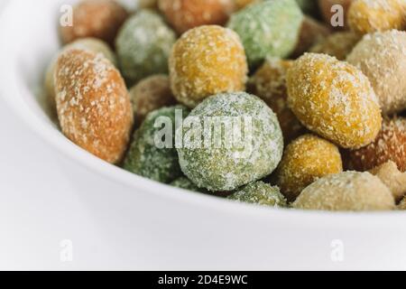 Salted peanuts covered with glaze in a ceramic bowl on a white background. A snack on the way. Delicious appetizer. Macro. Selective focus. Copy space Stock Photo