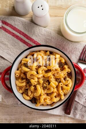 Bowl of macaroni and cheddar cheese with bacon pieces and glass of milk on a wooden table.  Overhead view Stock Photo