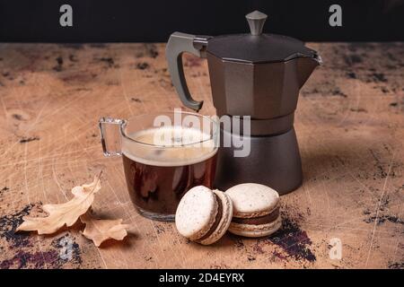 Coffee maker, cup of coffee and chocolate macarons on wooden background. Cozy autumn composition - Image Stock Photo