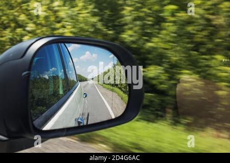 Rear view mirror of the car on outback road with blurred green forest in the background Stock Photo