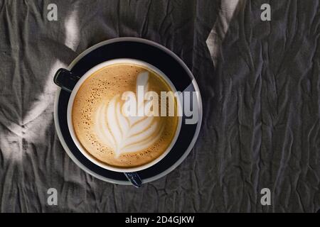 Coffee with latte art on grey linen tablecloth in natural sunlight, top view Stock Photo