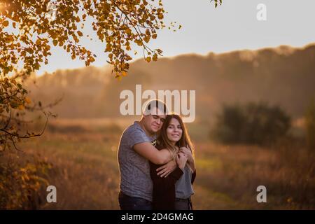Happy lovers hold hands, hug each other, kiss, spend time together. A young man and a girl are walking in the autumn forest.  Traveling Couple in love Stock Photo