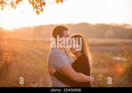 A young man kisses, hugs a beautiful smiling blonde woman with long hair. Close-up portrait of a couple embracing against the background of the autumn