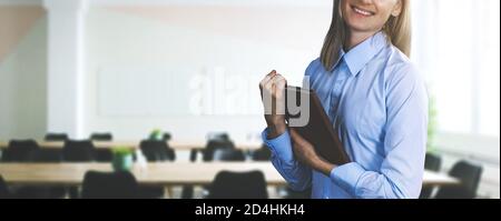 happy businesswoman in blue blouse holding tablet and standing on modern office background. banner copy space Stock Photo