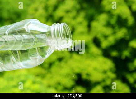 Drinking water drop out from plastic bottle with blurry green foliage in background Stock Photo