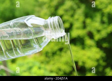 Drinking water pouring from a plastic bottle with blurry green foliage in the backdrop Stock Photo