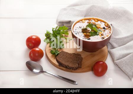 Vegetarian bean and olive soup in earthenware, rye bread, spoon and linen napkin on a white wooden table Stock Photo