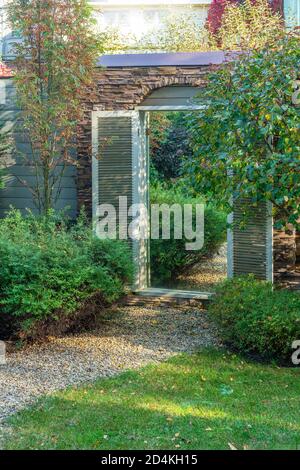 one of the landscape design techniques is the use of a mirror in the garden wall, which is framed like a door, which creates the illusion of a passage Stock Photo