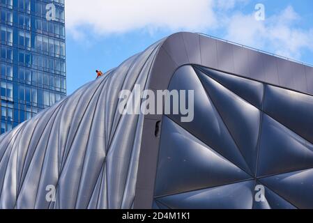 A maintenance worker in an orange shirt works on the roof of the Culture Shed at Hudson Yards, Manhattan, New York City Stock Photo