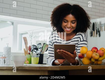 Beautiful female browsing recipe on digital tablet in the kitchen at home Stock Photo