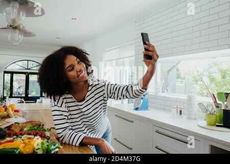 Young lady taking selfie in the kitchen, blogger and social media influencer  Stock Photo