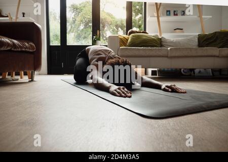 Young female stretching on yoga mat at home with wireless