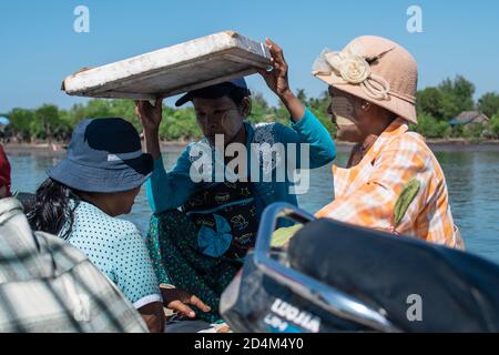 Chaung Thar, Myanmar - December 26, 2019: Portrait of three unidentified women with thanaka on their faces, one holds styrofoam for shade Stock Photo