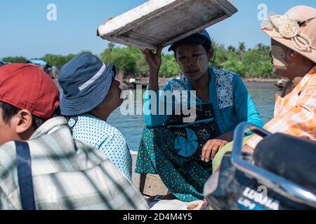 Chaung Thar, Myanmar - December 26, 2019: Portrait of three unidentified women with thanaka on their faces, one holds styrofoam for shade Stock Photo