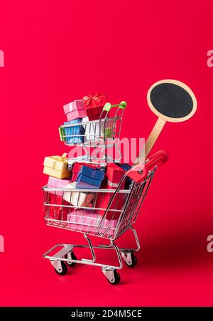 Christmas shopping concept with a shop cart full of gifts and an empty sign for sale and discount. Shopping cart with gifts isolated on red background Stock Photo