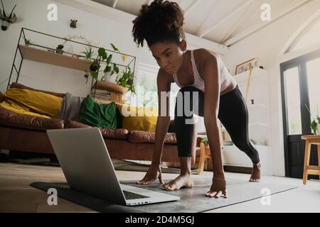 Beautiful young mixed race woman working out from home, online workout on laptop Stock Photo