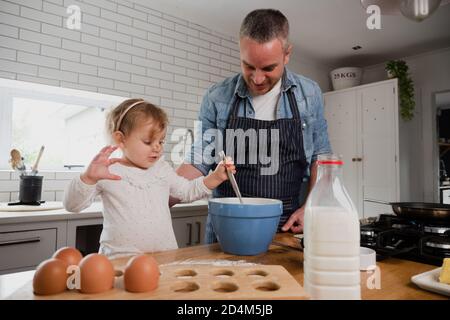 Father and kid daughter mixing ingredients in bowl together, in kitchen at home Stock Photo